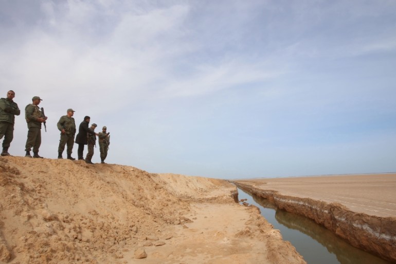 Soldiers overlook a trench, that forms part of a barrier along the frontier with Libya, in Sabkeht Alyun