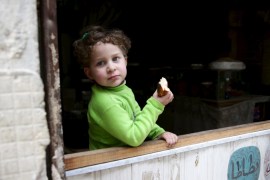 A child eats bread as she stands in front of a shop in the rebel held Qaboun neighborhood of Damascus, Syria [Reuters]