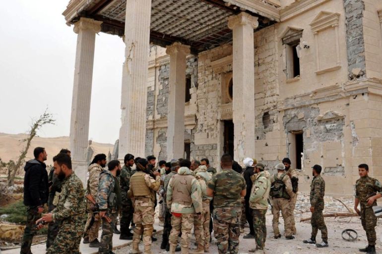 Syrian government soldiers gather outside a damaged palace, in Palmyra