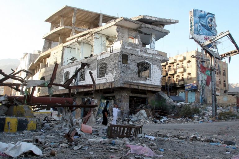 People walk past a building destroyed during recent fighting in Yemen''s southwestern city of Taiz