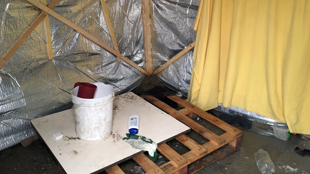 A bucket and measuring jug serve as a makeshift shower for the Bidoon in Calais [Shafik Mandhai/Al Jazeera]