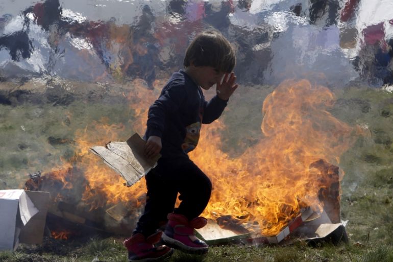 A refugee boy passes by cardboard boxes set on fire by other children, at the transit center for refugees near northern Macedonian village of Tabanovce on the border with Serbia [AP]
