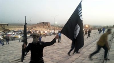 An ISIL fighter holds an ISIL flag and a weapon on a street in the city of Mosul, Iraq [REUTERS]