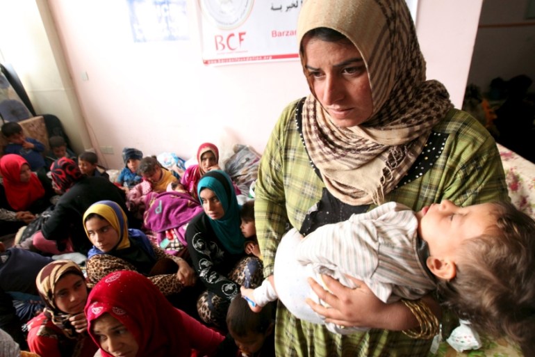A displaced woman carries her child in a building that is used as a temporary shelter in Makhmour