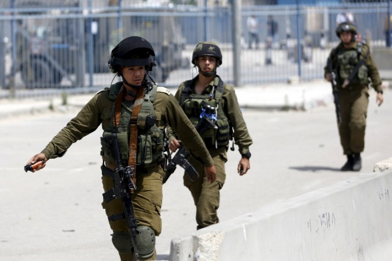 Israeli soldier prepares to throw a stun grenade towards Palestinian journalists near the scene where a Palestinian woman and a man, who the Israeli military said tried to stab