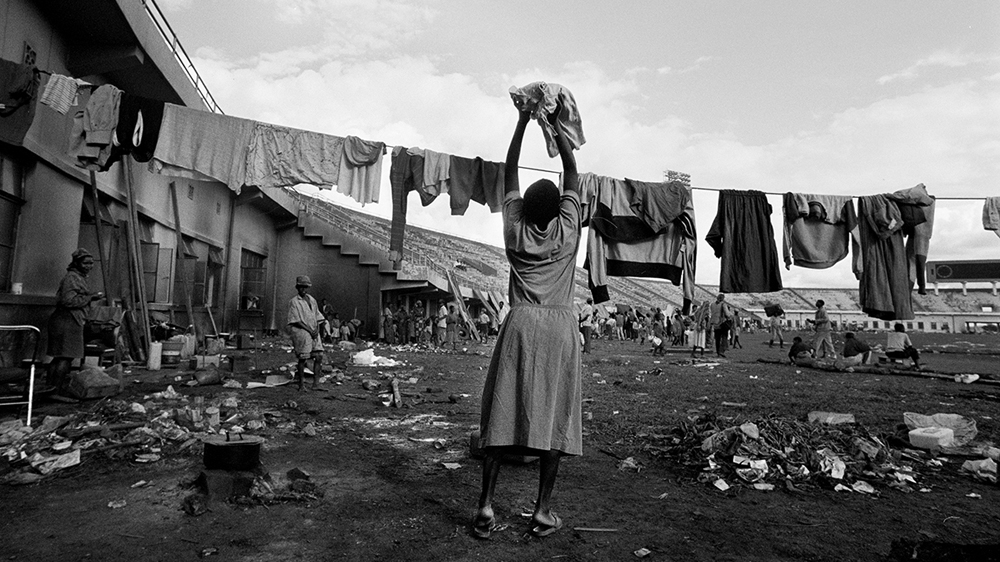 A woman hangs her washing to dry in a football stadium in Kigali as the shelling and killing continues outside [Jack Picone/Al Jazeera]