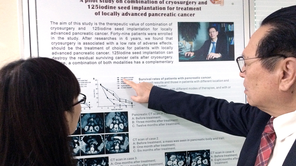 Xu Kecheng points to a poster describing one of Fuda Cancer Hospital's clinical trials [Simina Mistreanu/Al Jazeera]