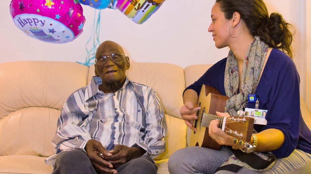 Fitzherbert Henderson, who just celebrated his 102nd birthday, closes his eyes and listens as Charla Burton, an MJHS music therapist, sings to him [Courtesy of MJHS]