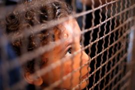 Boy looks through a fence as he waits with his family for a travel permit