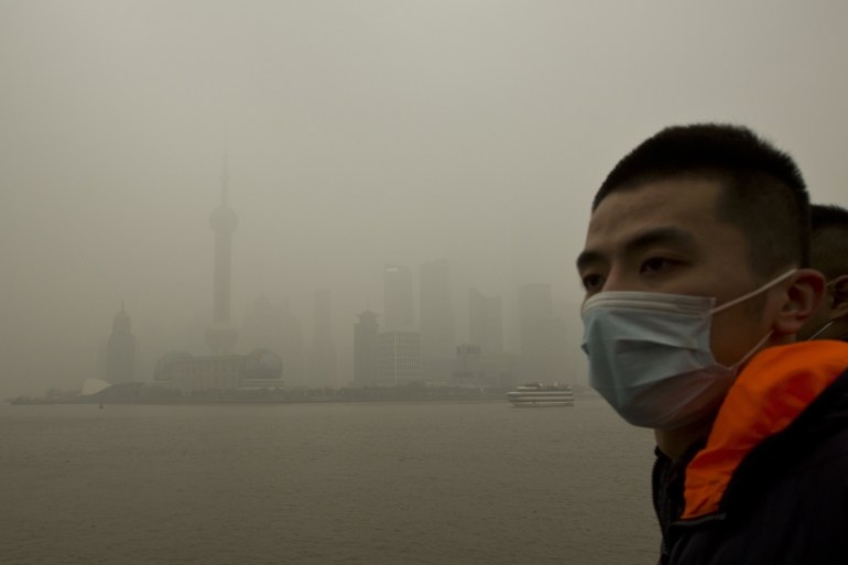 A man wears a face mask while walking on the Bund in front of the financial district of Pudong during a hazy day in downtown Shanghai