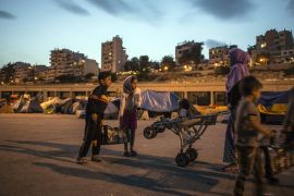 A family of Syrians collect supplies at dusk against a background of the multi-storey apartment buildings that compose most of central and suburban Athens [Iason Athanasiadis]