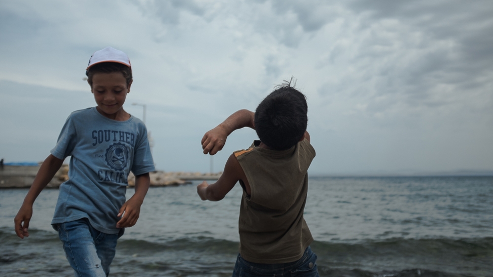 Young boys throw stones into the water at the Souda camp [Nick Paleologos/SOOC/Al Jazeera]