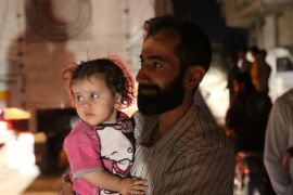 A man holds a child as he stands near a convoy carrying food supplies to deliver to the Syrian rebel-held town of Daraya in this handout picture provided by the World Food Programme