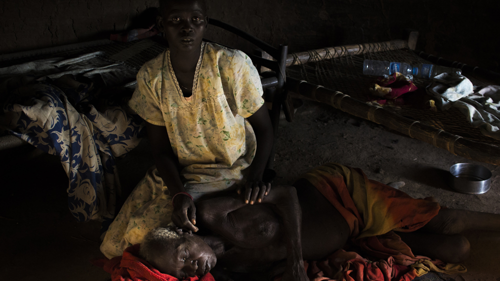 Abang Akok lies on the floor of her family home as one of her daughters brushes flies from her [Henry Wilkins/Al Jazeera] 