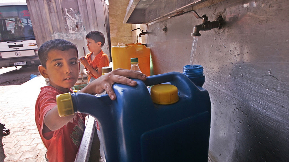 A Palestinian boy pours water into a container from a desalination plant [File: Ibrahim Khatib/Pacific Press/LightRocket via Getty Images]