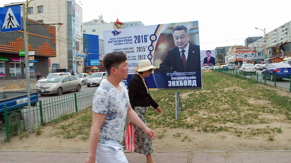 Mongolians walk past an election poster featuring Enkhbold Zandaakhuu, chairman of the ruling Democratic Party and speaker of parliament [Ganbat Namjilsangarav/Al Jazeera]