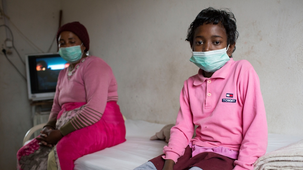 Hortence Modesstina, who has HIV and TB, in the hospital room in which she is quarantined with her mother, Bao. Both wear face masks to prevent visitors catching TB [Tom Maguire/Al Jazeera] 