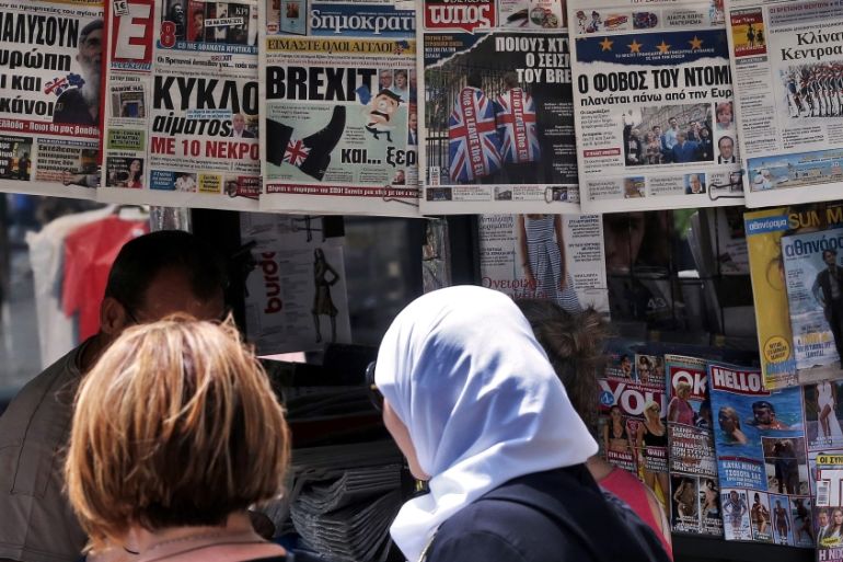 People glance at the frontpages of Greek newspapers hanging on a kiosk in central Athens, Greece [EPA]