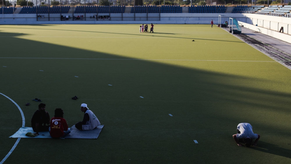 A man prays while others rest on the pitch of the abandoned Olympic stadium [Nick Paleologos/SOOC/Al Jazeera]