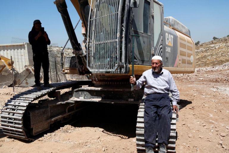 A Palestinian man sits on a tracks of an Israeli excavator as he tries to prevent it from clearing his land during a protest against Jewish settlements, near the West Bank city of Ramallah [REUTERS]