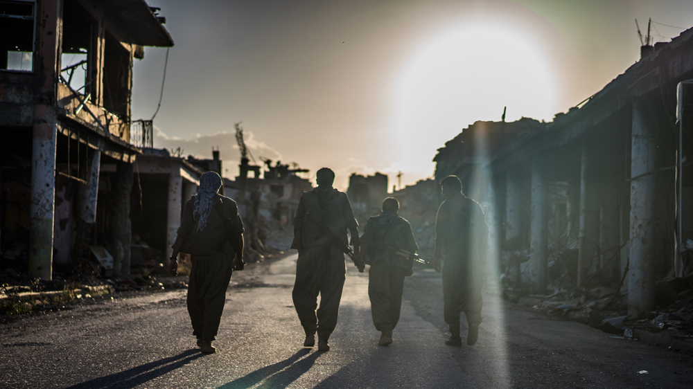 Four Kurdish guerrilla fighters make their way through the ruins of Sinjar [John Beck/Al Jazeera]