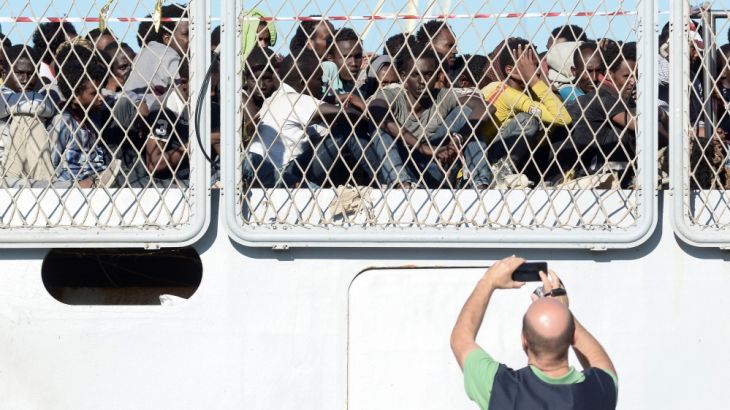 A police officer uses a mobile phone as migrants wait to disembark from the Italian Navy ship Borsini in the Sicilian harbour of Palermo