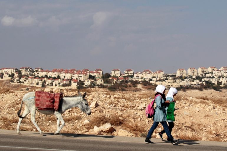 Palestinian schoolgirls walk with a donkey as a West Bank Jewish settlement is seen in the background [REUTERS]