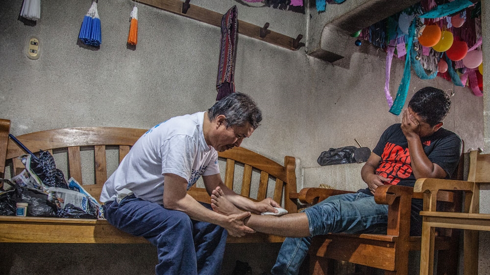 With his 'material' in hand, Don Juan massages Juan Ramirez's leg where it is injured [Gabriela Campos/Al Jazeera]