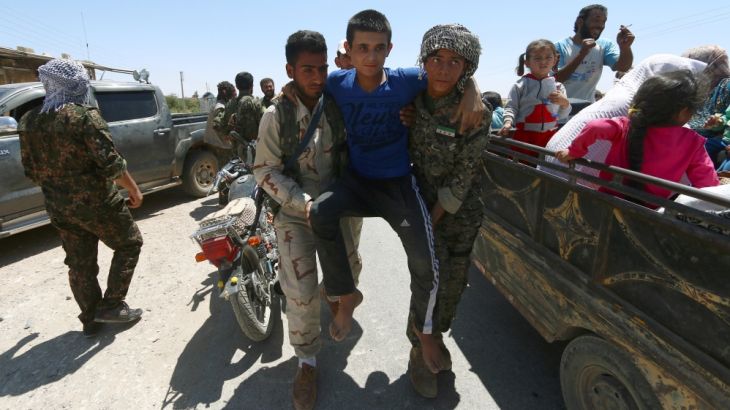 Syria Democratic Forces (SDF) fighters help an injured civilian as residents on pick-up trucks evacuate from the southern districts of Manbij city after the SDF advanced into it in Aleppo Governorate