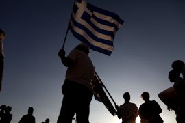A protester holds a Greek flag as he takes part in an anti-government rally organised to mark a year since Greeks voted against bailout measures in a referendum, in Athens, Greece [EPA]