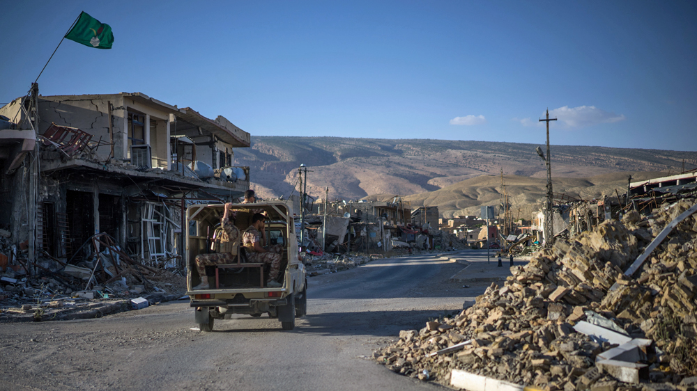 A truck carrying Kurdish security forces makes its way through the ruins of Sinjar [John Beck/Al Jazeera]
