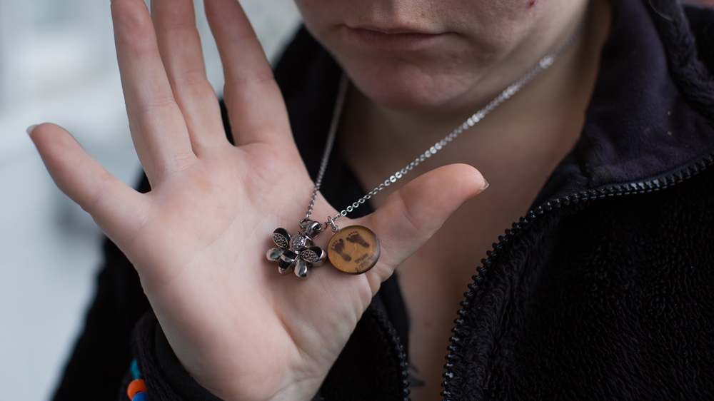  Tiffany shows the necklace that reminds her of her late daughter. The bee holds her daughter's ashes, while the other charm has small designs of her daughter's footprints  [Carolyn Bick/Al Jazeera] 