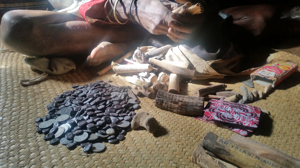 Traditional healer Mbola Tohamana uses seeds, mixed in a pile with coins, playing cards, some bones, a bracelet and small pieces of wood to diagnose ailments [William Worley/Al Jazeera]