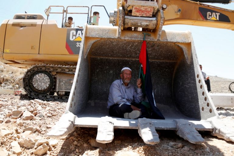 A Palestinian protests as he sits in the scoop of an Israeli excavator as tries to prevent it from clearing his land during a protest against Jewish settlements, near Ramallah [REUTERS]