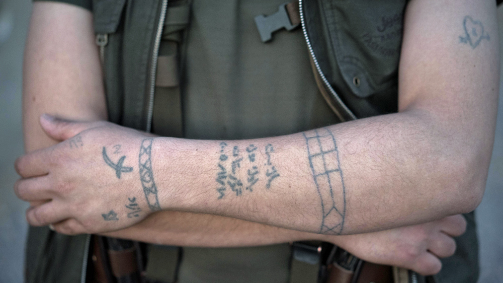 A Kurdish Peshmerga fighter shows off his homemade tattoos at an active front line position outside Sinjar [John Beck/Al Jazeera] 