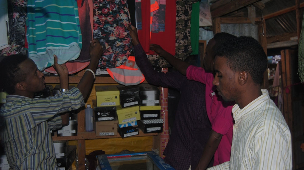 Deck Yusuf Mohamed, left, attends to customers at his family's shop in Ifo refugee camp [Anthony Langat/Al Jazeera]