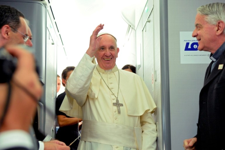 Pope Francis waves next to newly-retired Father Federico Lombardi during a press conference on a plane after the Pope''s visit to Krakow for the World Youth Days