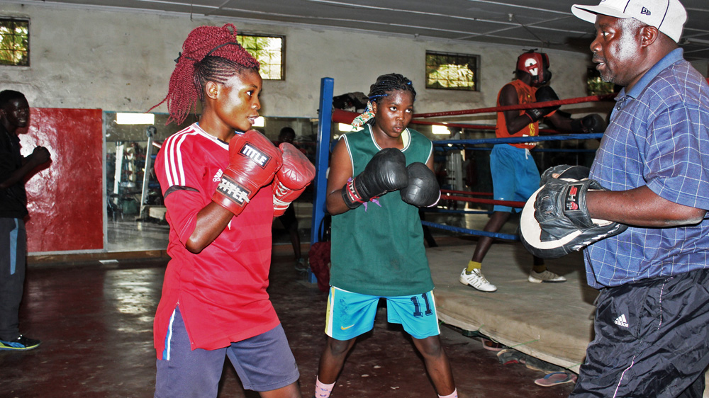 Margaret Tembo, 16, and Alice Mbewe, 17, both members of Zambia's national boxing team, face their trainer, Ariel Banda [Tendai Marima/Al Jazeera]
