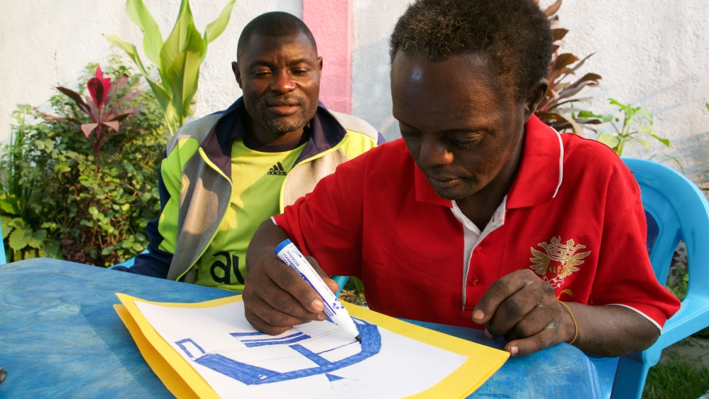 Raymond Mafuala, left, watches his brother Blaise Kanza draw. The family is supportive of Blaise's passion for art [Kait Bolongaro/Al Jazeera]