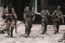 Syria Democratic Forces (SDF) fighters walk on the rubble of damaged shops and buildings in the city of Manbij
