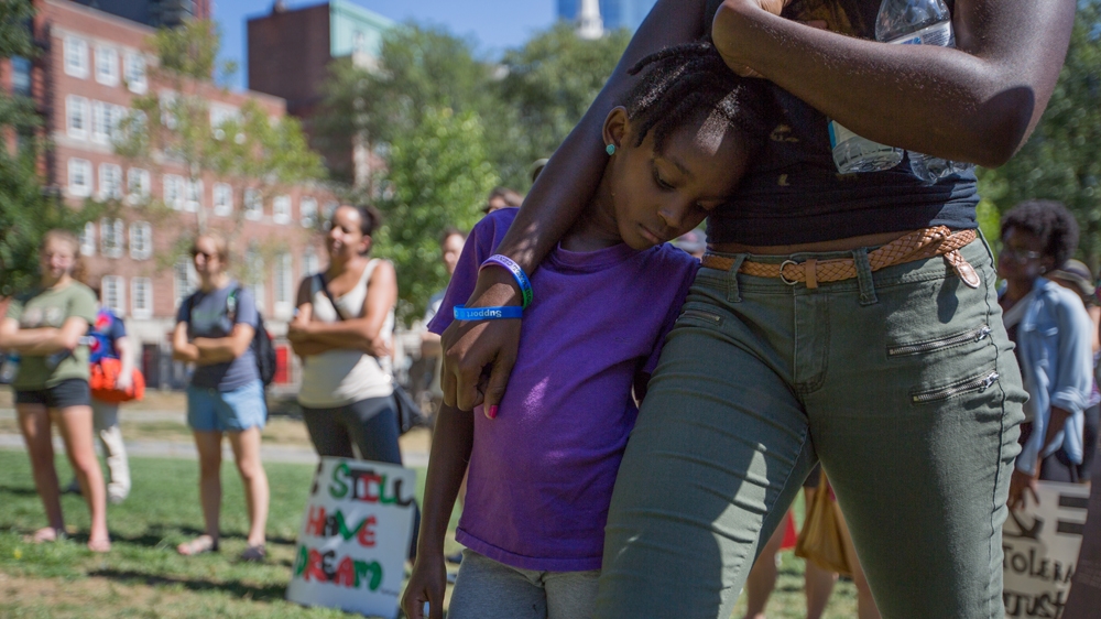 Bria Small, centre, leans against her sister, Naria Sealy, as they listen to Rahsaan Hall speak   [Carolyn Bick/Al Jazeera]  