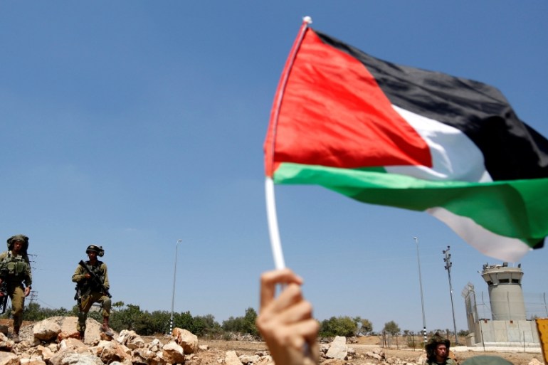 Demonstrator waves a Palestinian flag in front of Israeli soldiers during a protest in solidarity with Palestinian prisoners held in Israeli jails, in the West Bank village of Nabi Saleh