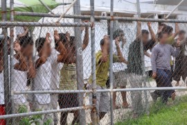 Asylum seekers look at the media from behind a fence at the Manus Island detention centre, Papua New Guinea