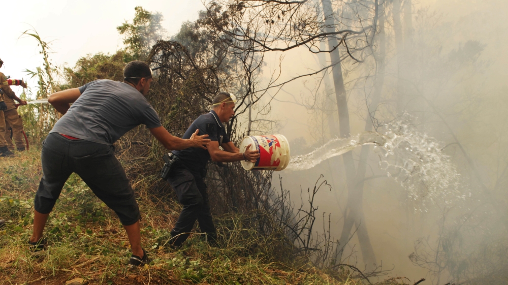 Civilians and police officers used water buckets to help extinguish the forest fire near houses at Sao Joao Latrao, Funchal. [Duarte Sa/ Reuters]