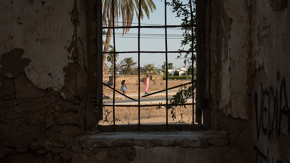 Children playing on the street can be seen through the window of a deserted church in Famagusta [Wojtek Arciszewski/Al Jazeera]