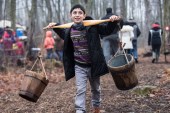A Syrian refugee child carries buckets used in the making of maple syrup in Mississauga, Canada [Getty]