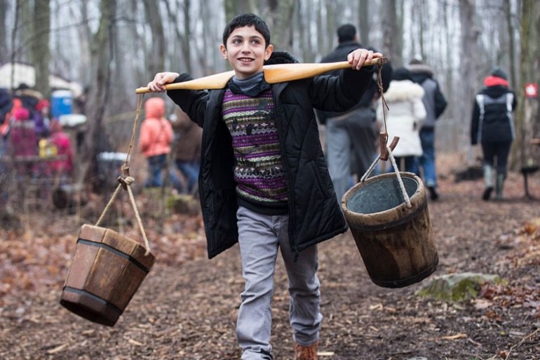 A Syrian refugee child carries buckets used for making maple syrup in Mississauga, Canada [Getty]