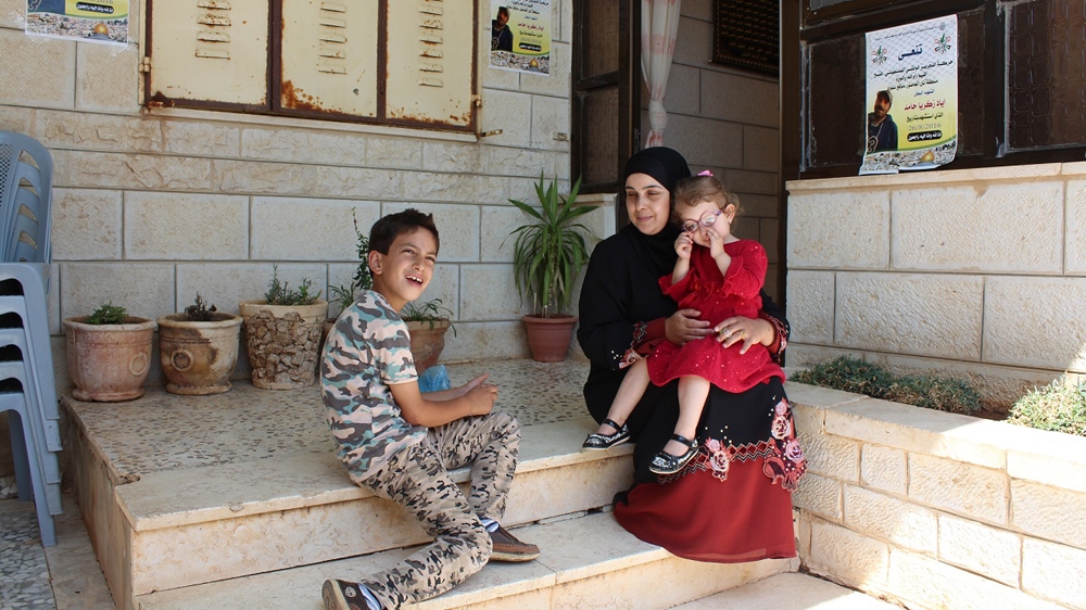 Zakaria, Iyad's son, and Layan, his daughter, sit with their aunt outside the family home, underneath posters remembering Iyad [Nigel Wilson/Al Jazeera] 
