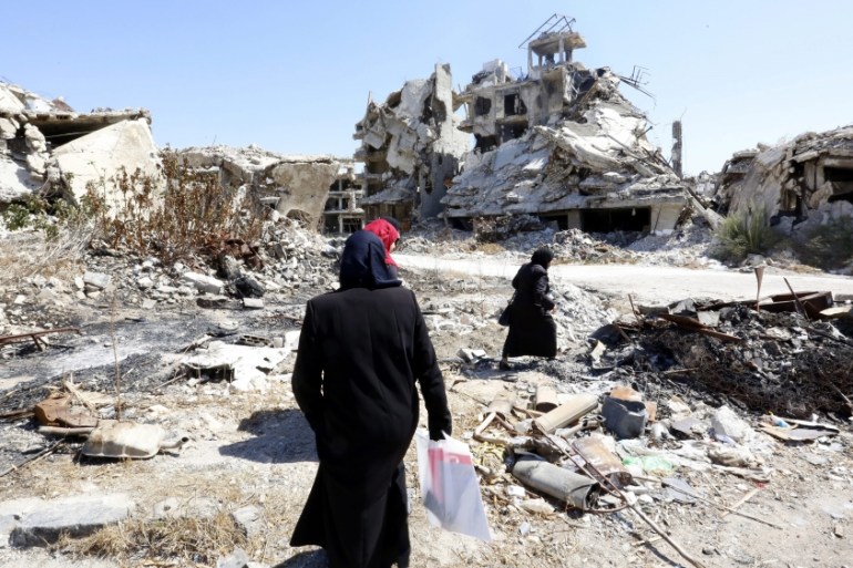 People walk between rubble in the city of Homs, Syria [EPA]