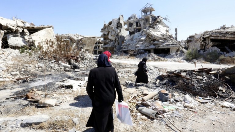 People walk between rubble in the city of Homs, Syria [EPA]